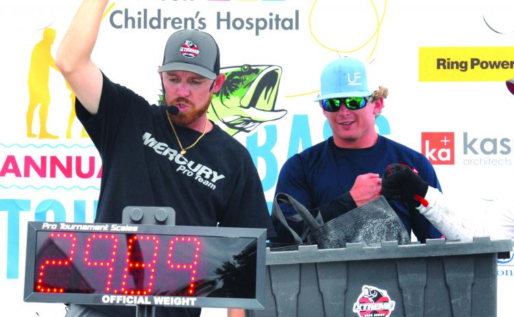 Tournament emcee Brian Stahl raises his fist to announce the winning weight for Austin Black, right, and partner Wyatt Kenney at Saturday’s Wolfson Children’s Hospital Bass Tournament at Palatka Dockside. (GREG WALKER / Daily News correspondent)